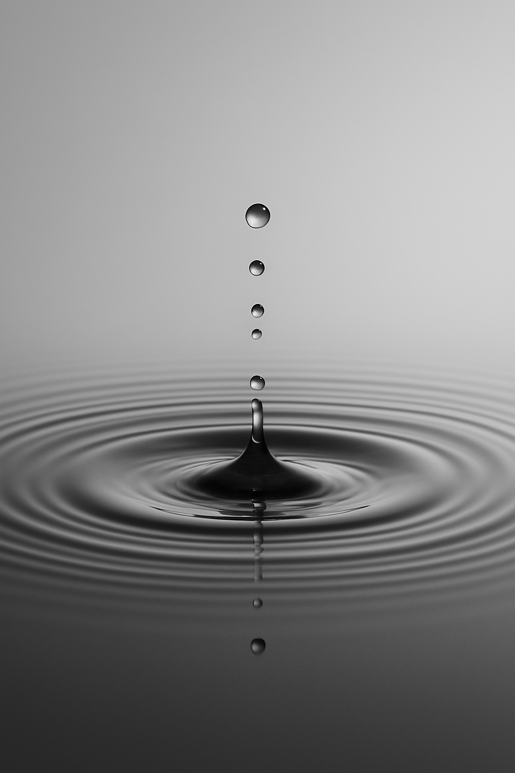 Schwarz-weiss Fotografie eines fallenden Wassertropfens, der eine glatte Oberfläche trifft und konzentrische Wellen erzeugt. Minimalistisch, ruhig, modern.